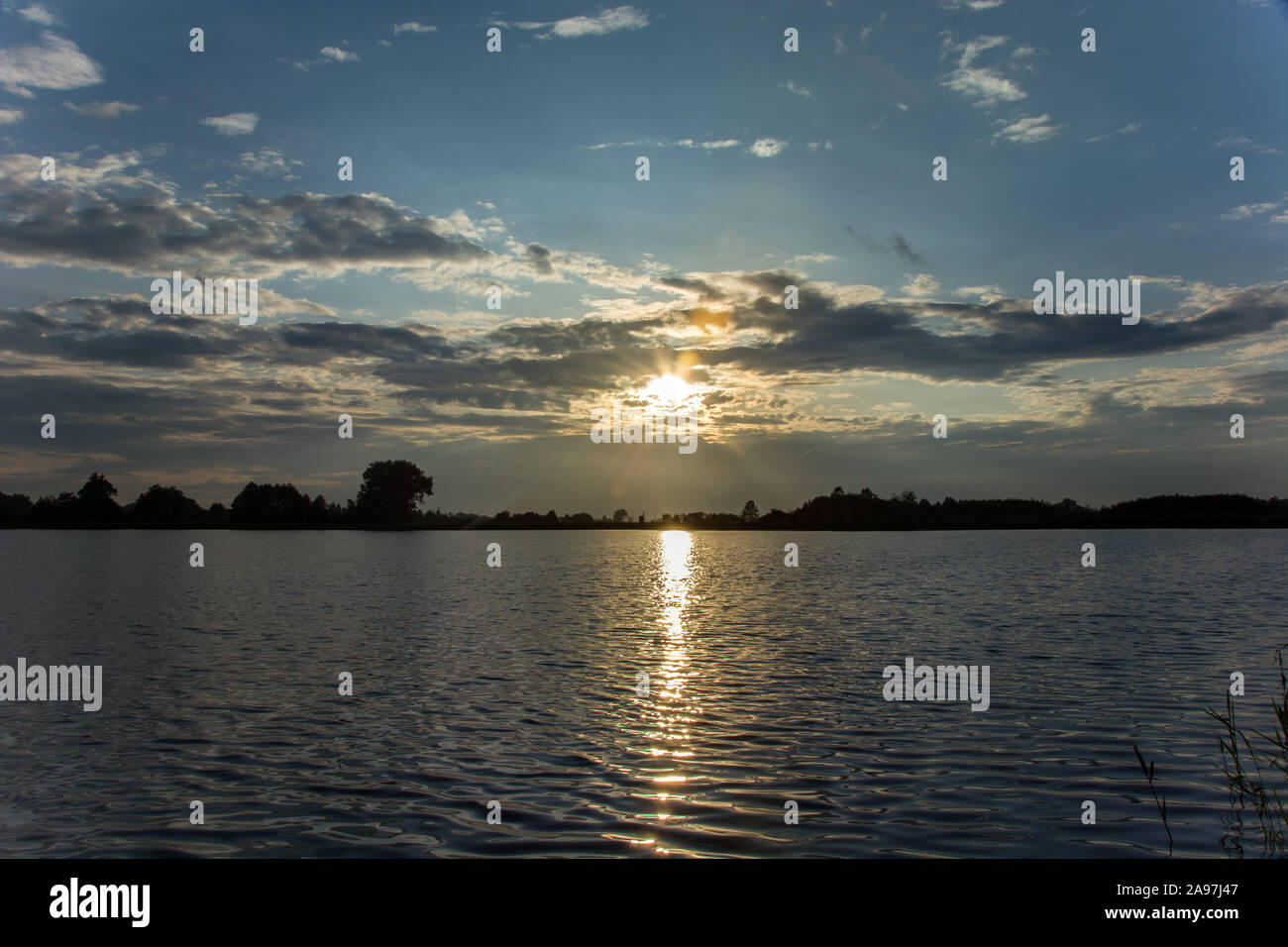 Sun tra le nuvole e riflettendo la luce nelle acque del lago - vista serale in Stankow, Lubelskie, Polonia Foto Stock