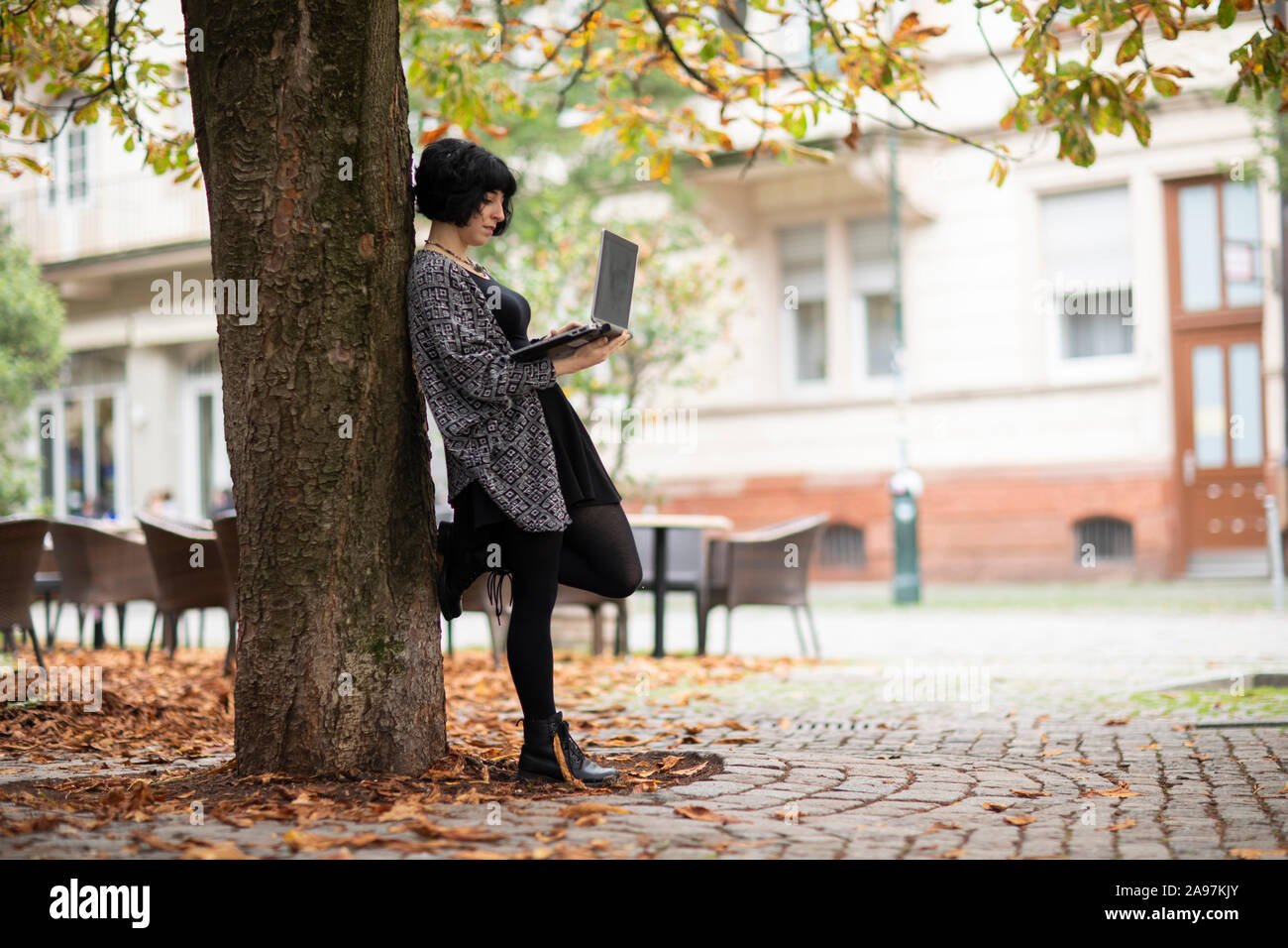 Giovane donna con il computer portatile al di fuori a lavorare vicino a un albero Foto Stock
