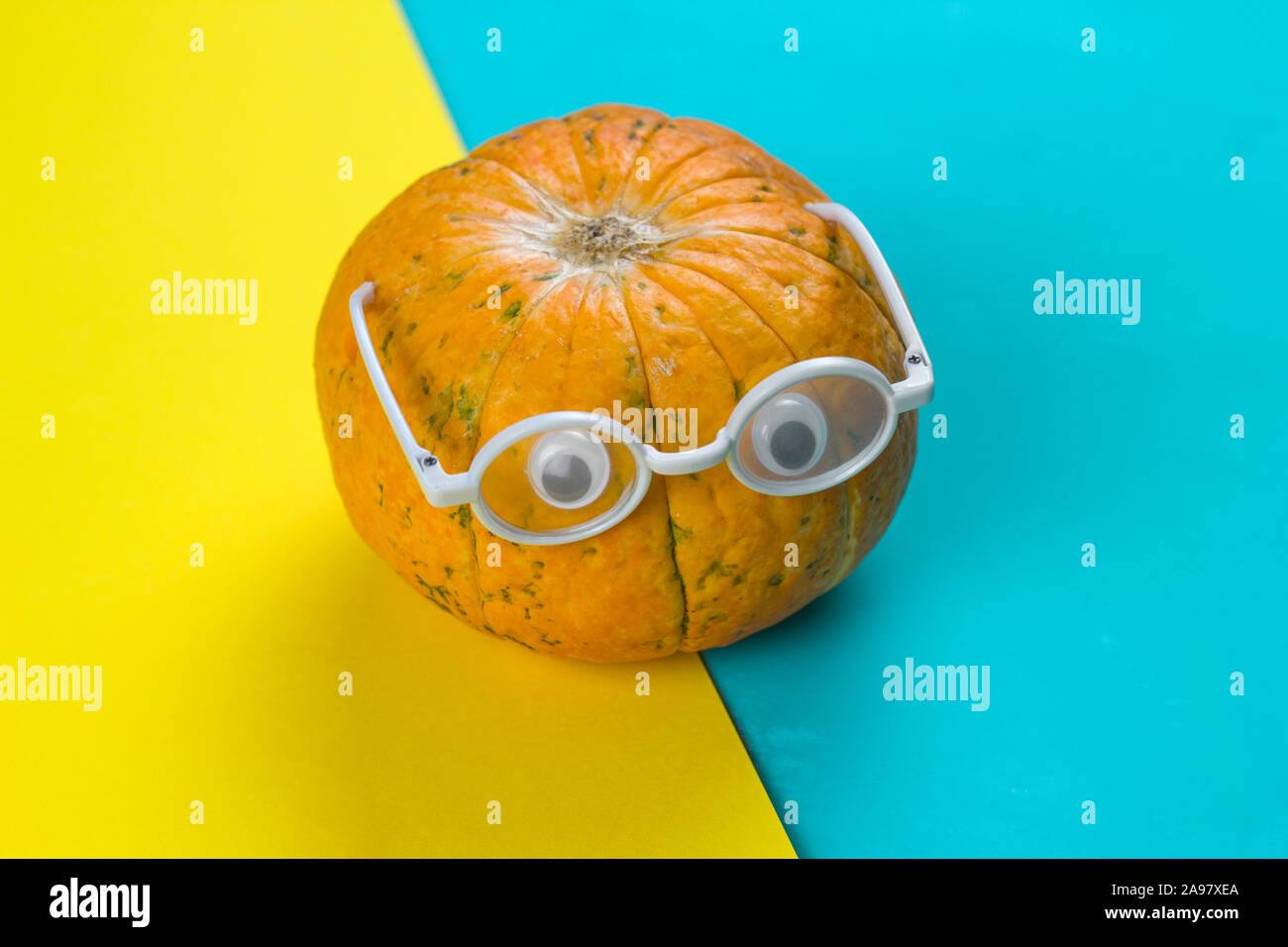 Poco divertente zucca con gli occhi con gli occhiali su un giallo e sfondo blu Foto Stock