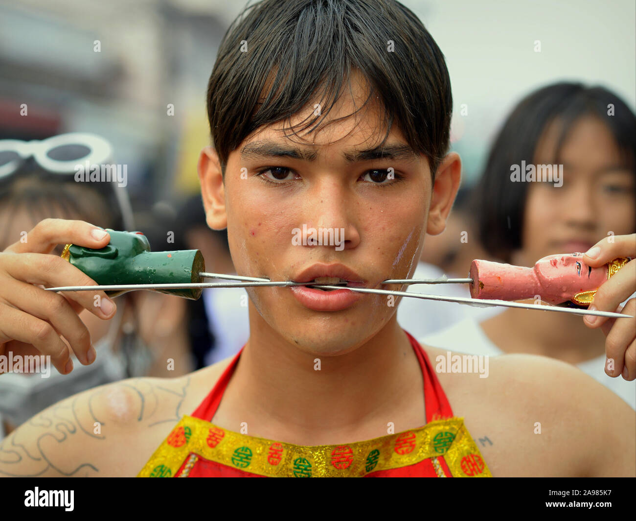 Giovani Thai cinese taoista devoto perfora le sue guance con perni lunghi/spiedini durante il Phuket Vegetarian Festival (nove imperatore dèi Festival). Foto Stock