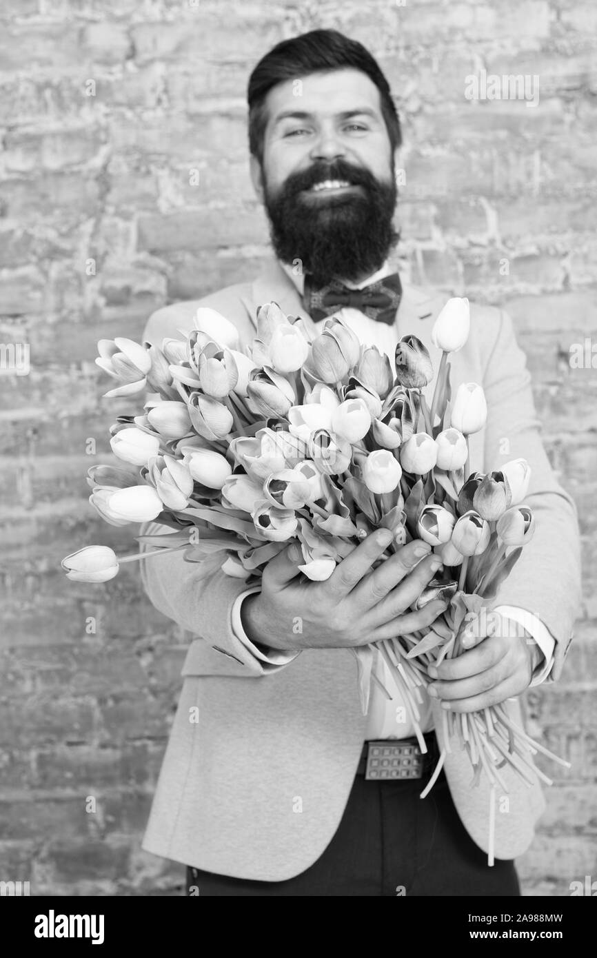 Uomo romantico con fiori. Regalo romantico. Macho getting ready data romantico. I tulipani per sweetheart. L'uomo ben curato usura smoking blu bow tie tenere bouquet di fiori. In attesa che la sua fidanzata. Foto Stock