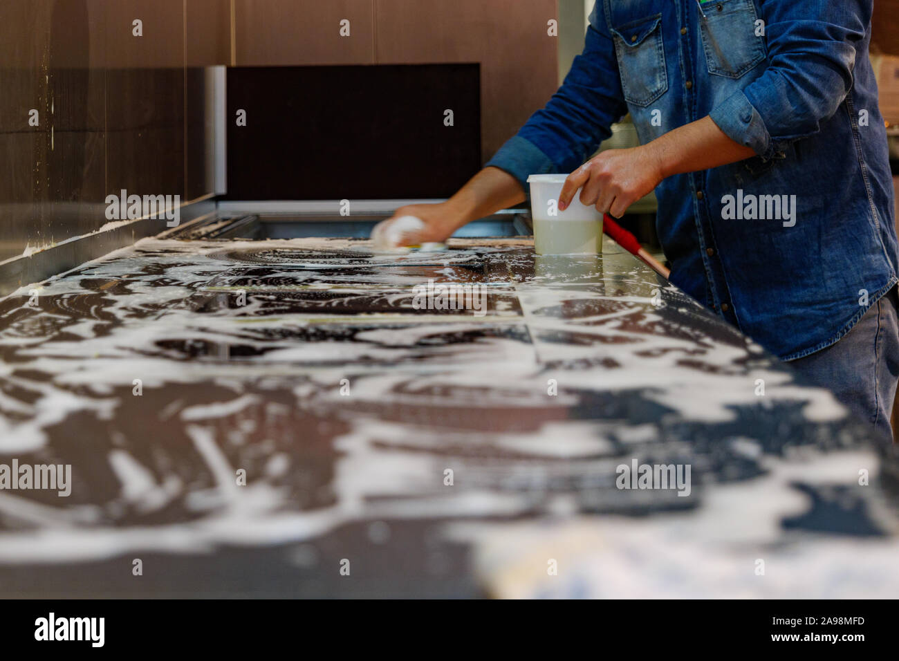 Pulizia del dipendente e asciugare la cucina della stazione di cottura su metallica o superficie in acciaio inossidabile con sapone, mop e spugna. Foto Stock