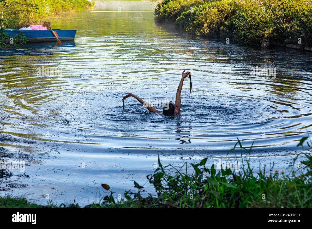 Strana persona godendo di una bella nuotata all'interno di un pool fossato pieno di sporcizia, mentre una barca a remi è in background Foto Stock