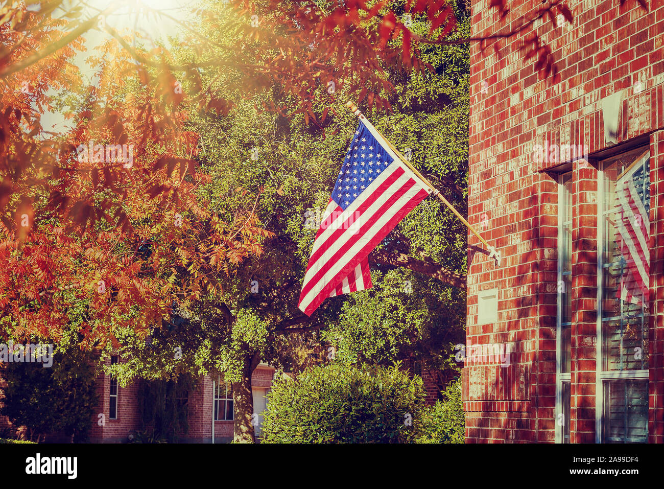 Patriottica bandiera americana sventola davanti a una casa di mattoni su una soleggiata giornata autunnale. Vintage effetti di filtro. Foto Stock