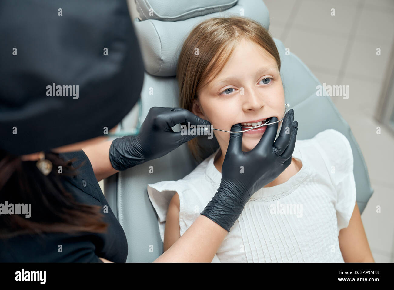 Giovane e bella ragazza in visita dal dentista nella moderna clinica dentale. Paziente seduto in poltrona odontoiatrica. Dottore in nero uniforme e nero guanti di gomma cercando le bretelle per l'allineamento dei denti. Foto Stock