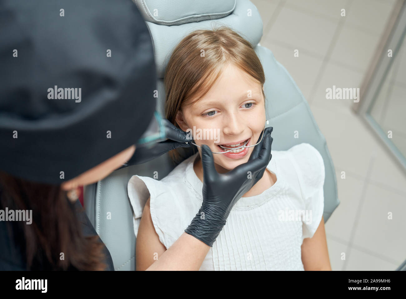 Bella ragazza seduta in poltrona odontoiatrica con bocca di apertura. Dentista in uniforme e nero guanti di gomma la diagnosi di denti per le parentesi graffe. Concetto moderno di stomatologia. Foto Stock