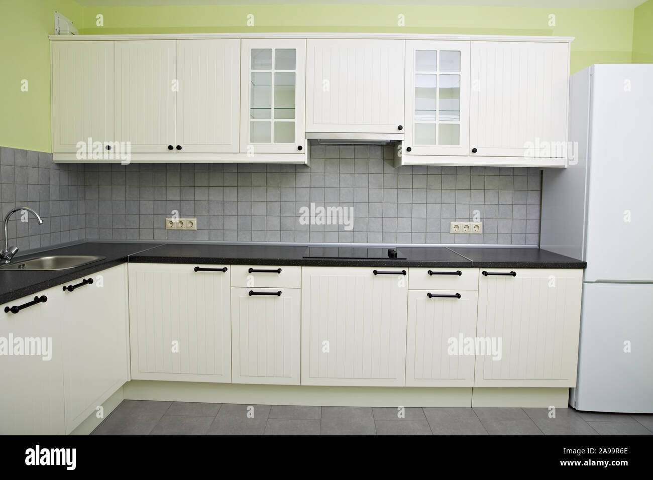 Moderna cucina bianca nell'appartamento. Frigorifero, piano cottura, lavello con rubinetto. Foto Stock