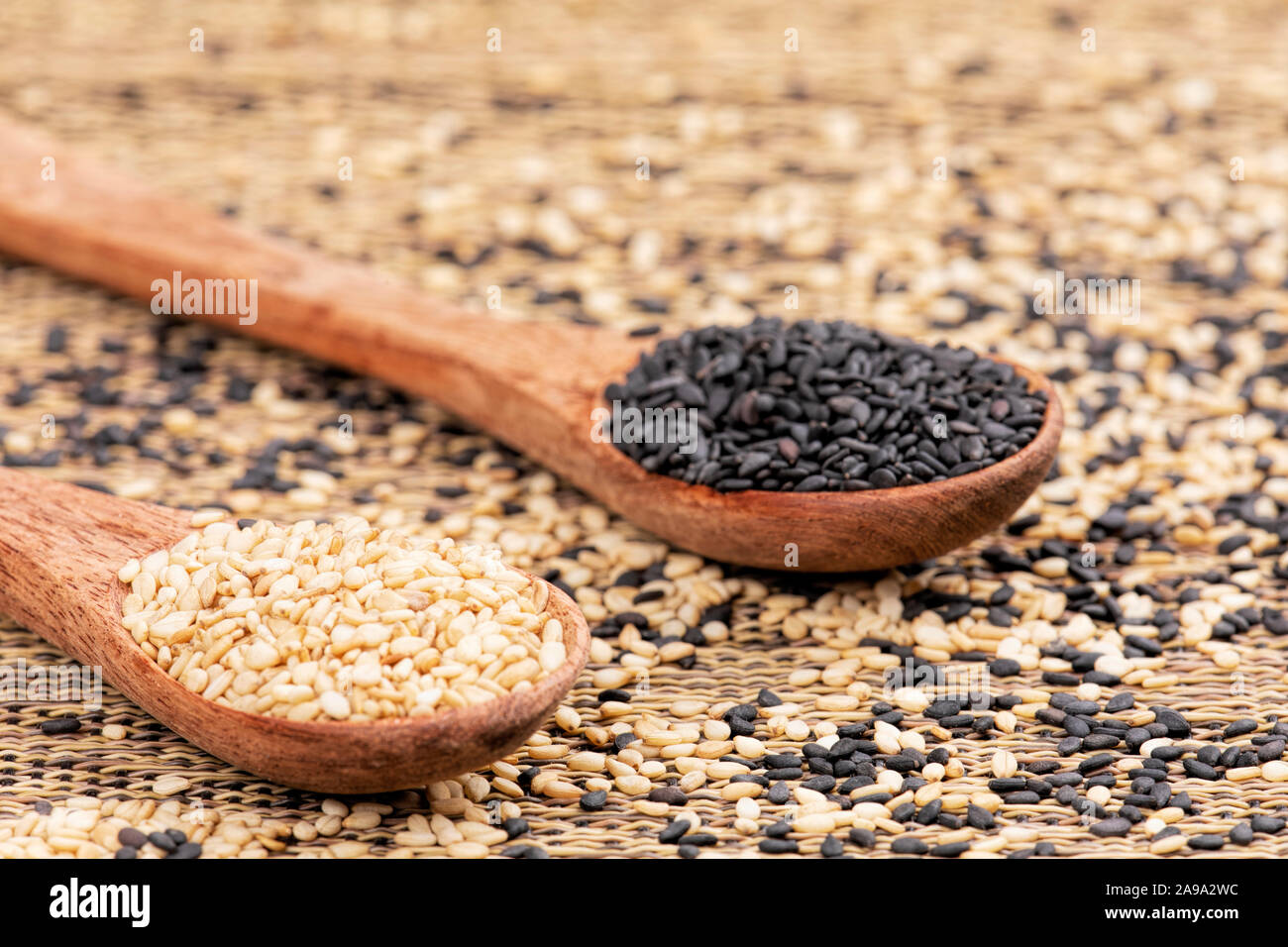 Cucchiai di legno pieno di sana e deliziosa di semi di sesamo e di semi di sesamo nero su uno sfondo a trama Foto Stock