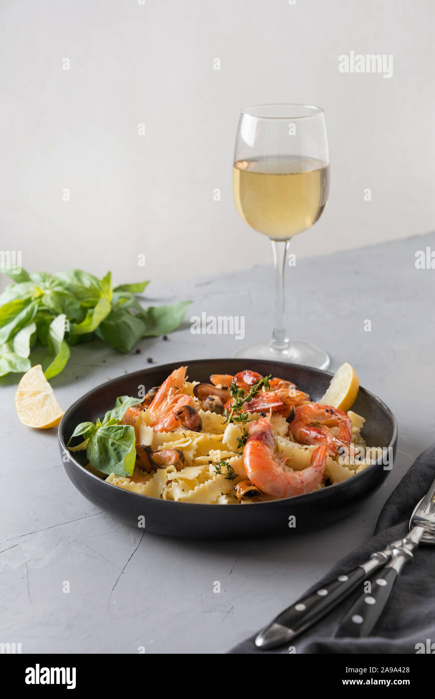 Reginelle Pasta con pesce, gamberi, cozze, bicchiere di vino bianco grigio sul tavolo di pietra, vicino. Piatto tradizionale nel ristorante italiano. Foto Stock