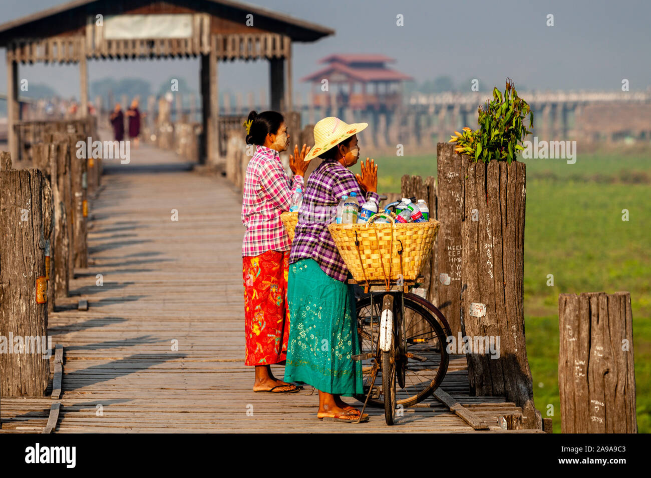 Due donne su biciclette Stop per pregare su U Bein Bridge, Amarapura, Mandalay Myanmar. Foto Stock