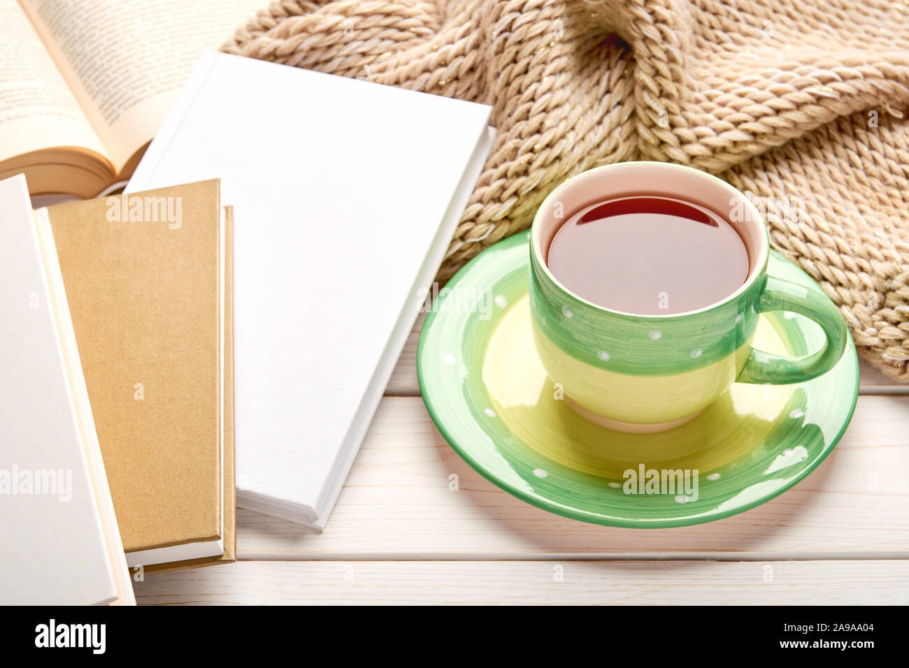 Ancora vita su bianco tavolo in legno alto. Green tazza di tè e la pila del libro in copertina rigida. Spazio per il testo. Foto Stock