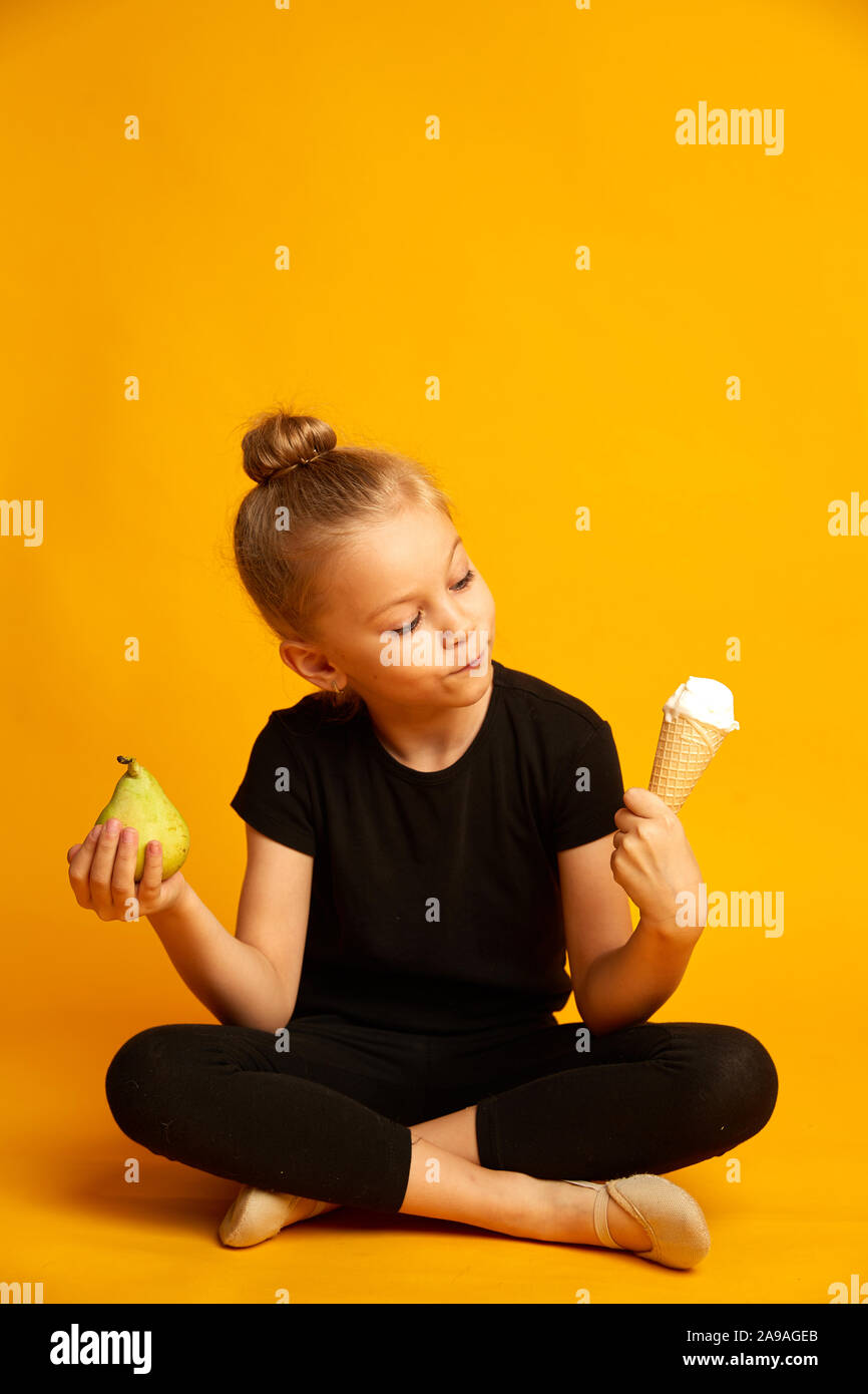 Perplesso little ballerina scegliendo tra pera e gelato Foto Stock