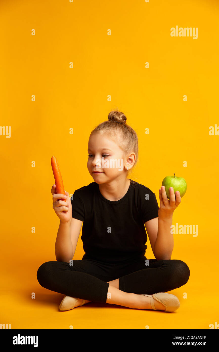 Perplesso little ballerina scegliendo tra carote e mela verde Foto Stock