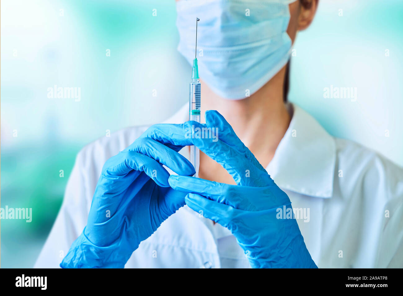 Medico donna o scienziato in bianco camice blu, guanti, cappuccio verde e la maschera contiene una siringa in mani su sfondo bianco. Ella è pronta a dare Foto Stock