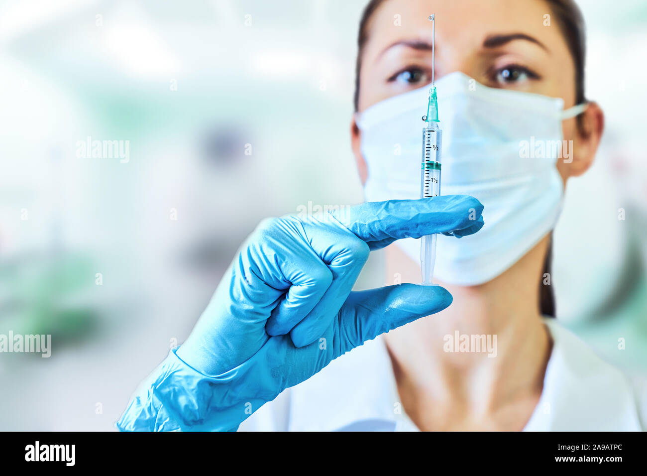 Medico donna o scienziato in bianco camice blu, guanti, cappuccio verde e la maschera contiene una siringa in mani su sfondo bianco. Ella è pronta a dare Foto Stock