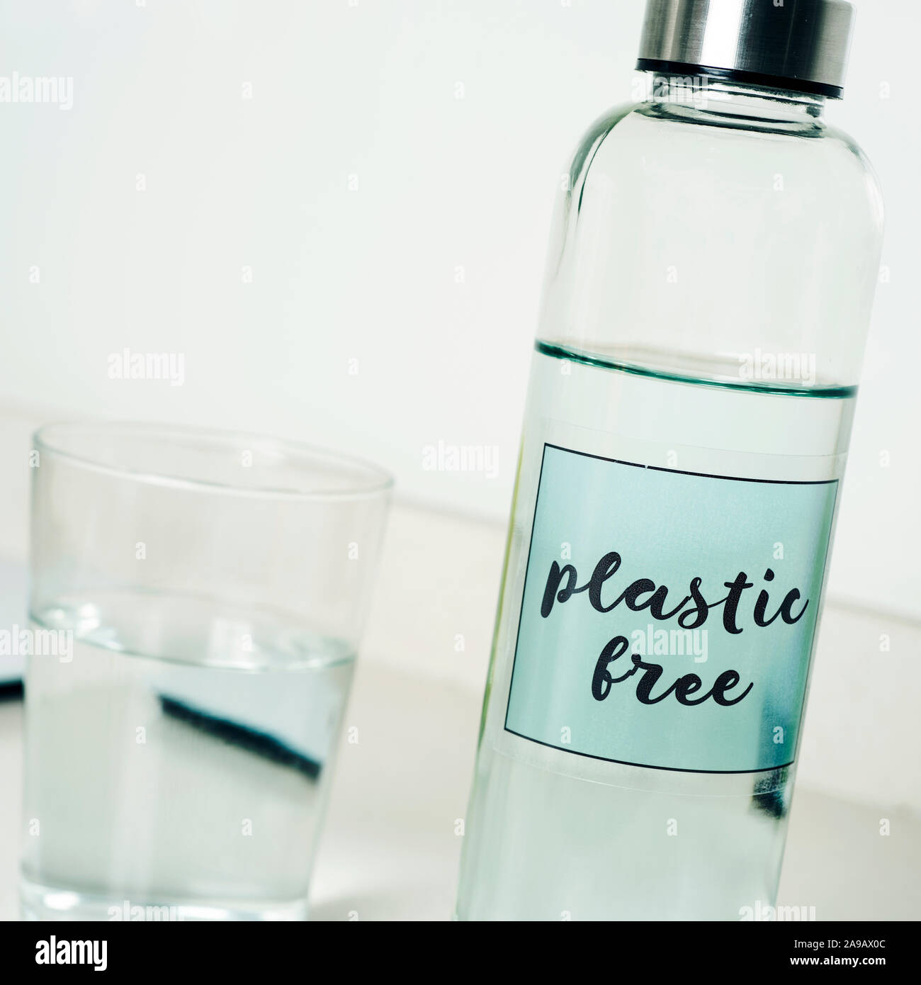 Primo piano di una riutilizzabili in vetro di acqua in bottiglia con il testo libero in plastica scritto in esso, su un tavolo bianco Foto Stock