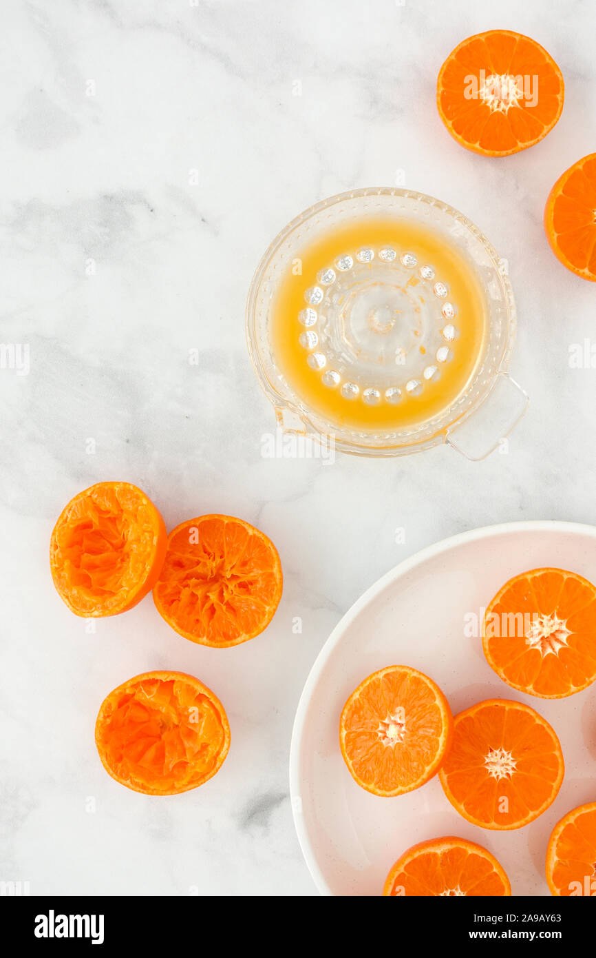 Metà delle clementine e strizzata clementine su lastra di marmo bianco e lo sfondo con spremiagrumi riempite con succo. Vista dall'alto. Foto Stock