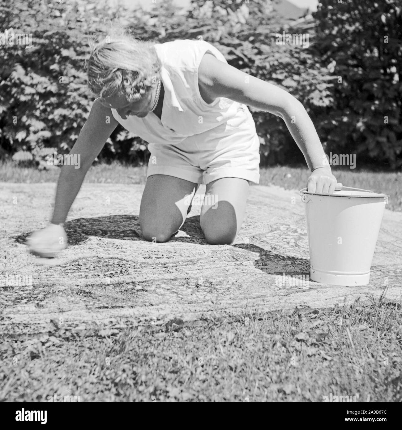 Una donna ha portato un tappeto al giardino per pulirlo, Germania 1958 Foto Stock