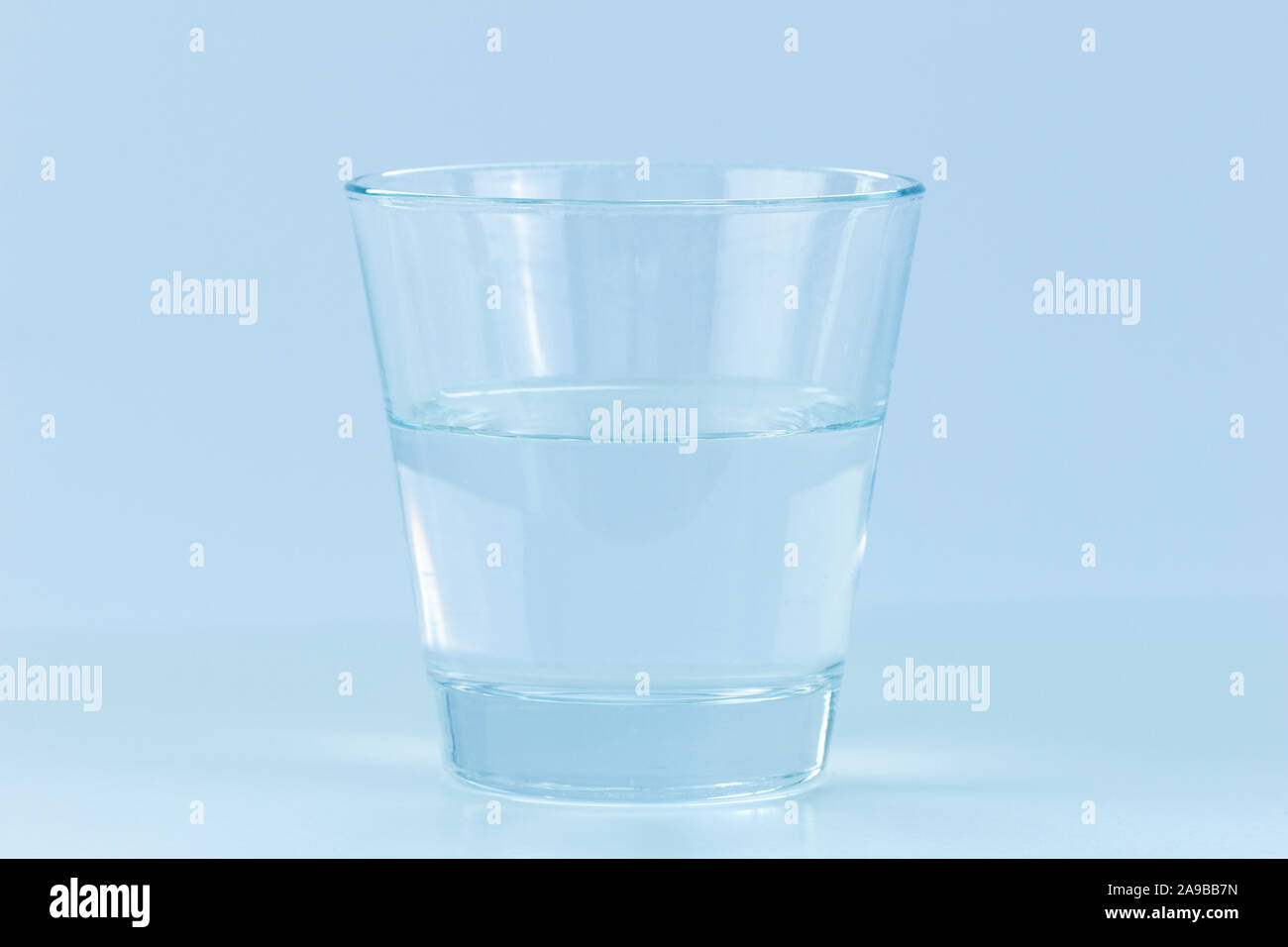 Close-up di un trasparente bicchiere mezzo pieno o vuoto di acqua. Concetto di foto o positivo atteggiamento negativo. Tonalità di blu. Foto Stock
