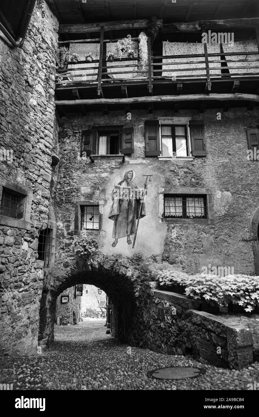 Via Fratelli Bandiera, corsia stretta attraverso archi a tunnel in colle medievale borgo di Canale di Tenno, Trentino-Alto Adige, Italia. In bianco e nero Foto Stock