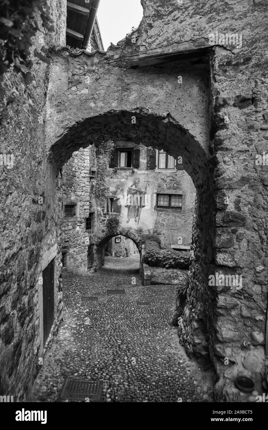 Via Fratelli Bandiera, corsia stretta attraverso archi a tunnel in colle medievale borgo di Canale di Tenno, Trentino-Alto Adige, Italia. In bianco e nero Foto Stock