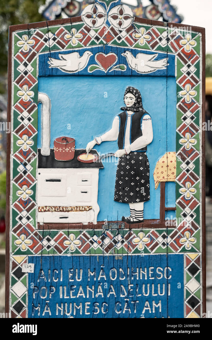Una croce di legno scolpita decorata in modo allegro segna la tomba di una casalinga nel famoso Cimitero Merry, nel villaggio di Săpânța, Maramureş, Romania Foto Stock