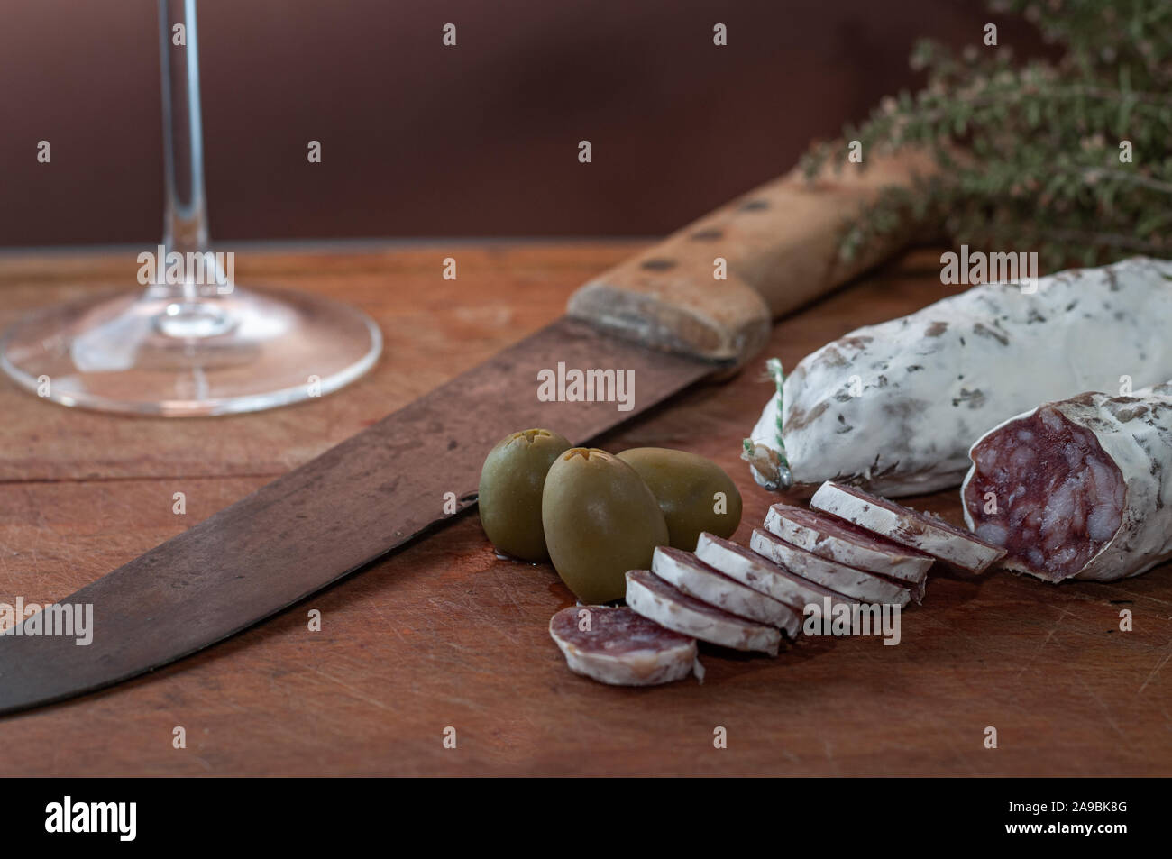 Francese salsiccia secca o salsiccia. sul tagliere con coltello e olive. Foto Stock
