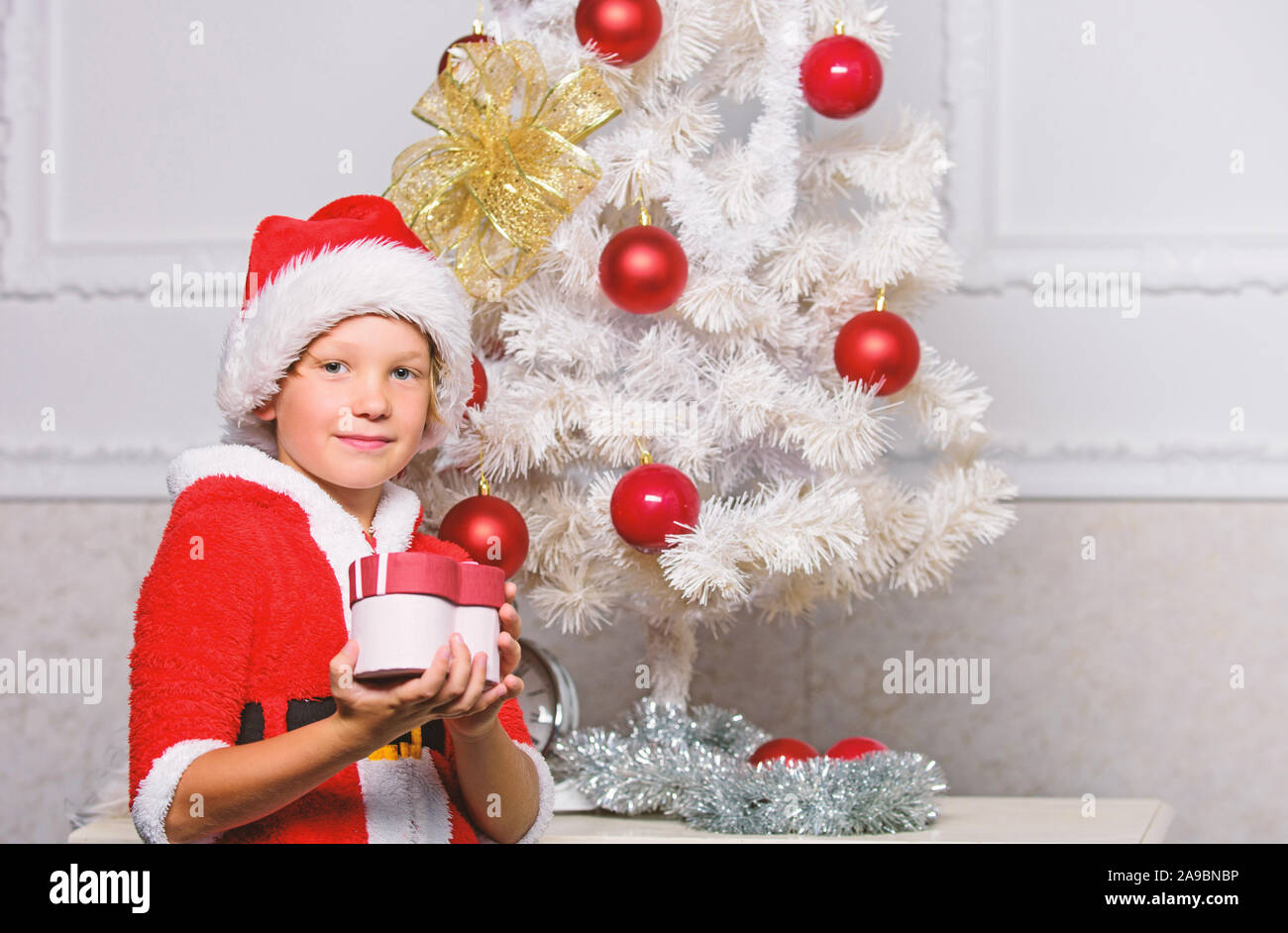 Albero di natale idee per i bambini. Boy kid vestiti come santa con Red Hat  tenere confezione regalo vicino albero di natale. Christmas Santa Claus  costume per bambino. Festa di Natale con