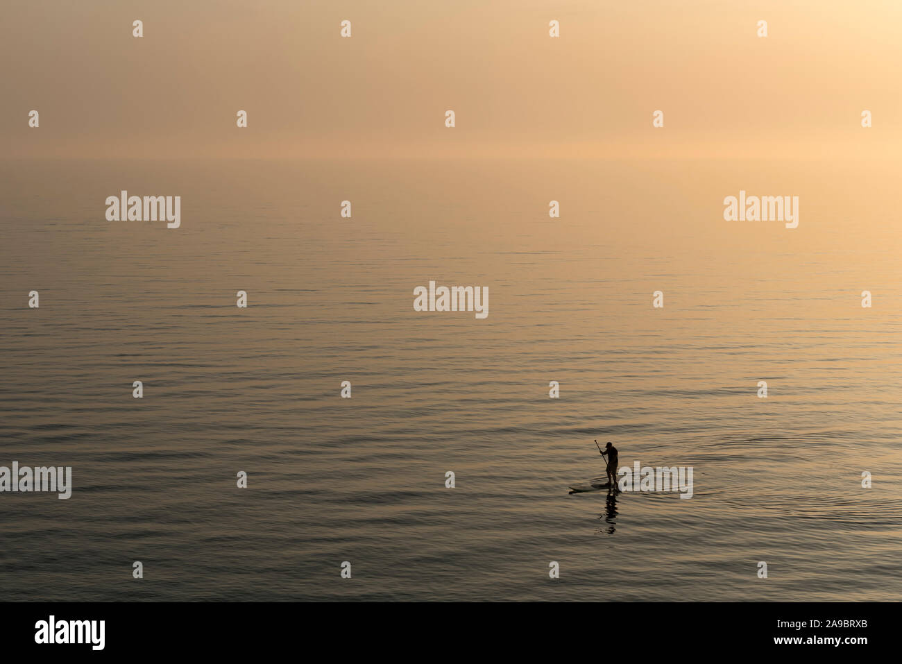 Uomo che pratica stand up paddle boarding sul mare dopo il tramonto Foto Stock