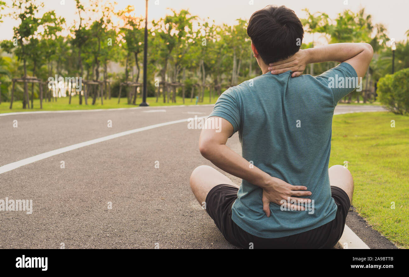 Un atleta maschio che soffrono di dolori al collo e alla schiena e di pregiudizio al parco. Lo sport e il concetto di assistenza sanitaria. Foto Stock