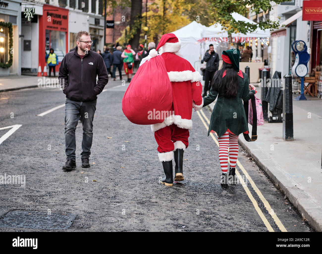 Babbo Natale e un Elfo femmina a piedi mano nella mano getting look dal passante sulla strada di Londra Foto Stock