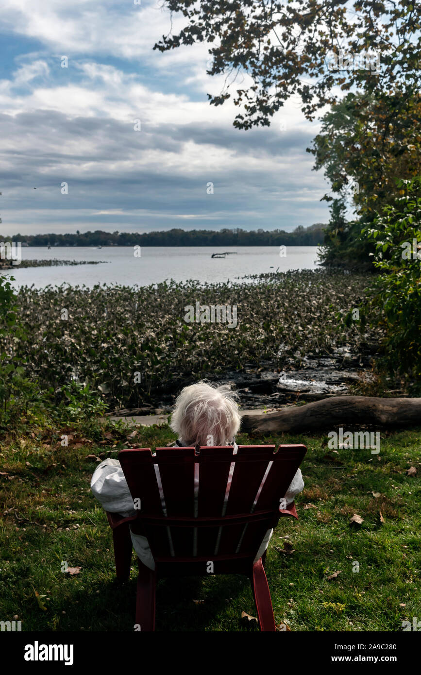 Una donna anziana si siede in una poltrona di legno in un parco vicino al fiume, Philadelphia, Pennsylvania, STATI UNITI D'AMERICA Foto Stock