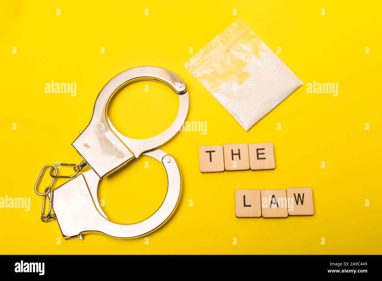 La criminalità o il concetto di giustizia che mostra un segno la lettura della legge su sfondo giallo con le manette e un pacchetto di farmaci Foto Stock