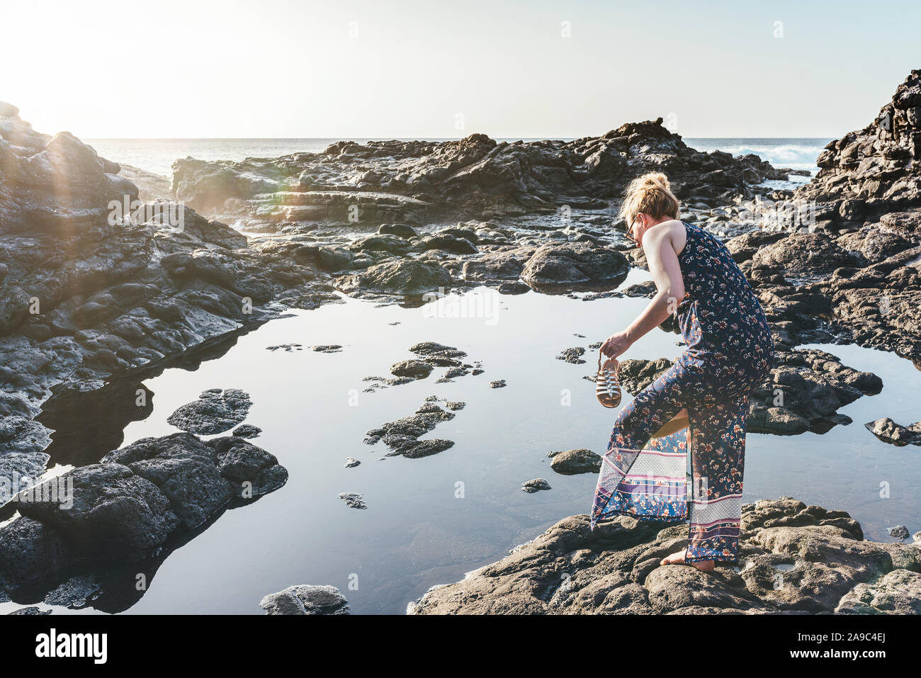 Blonde caucasian donna in abiti estivi di decollare le sue scarpe dall'oceano sulla giornata di sole Foto Stock