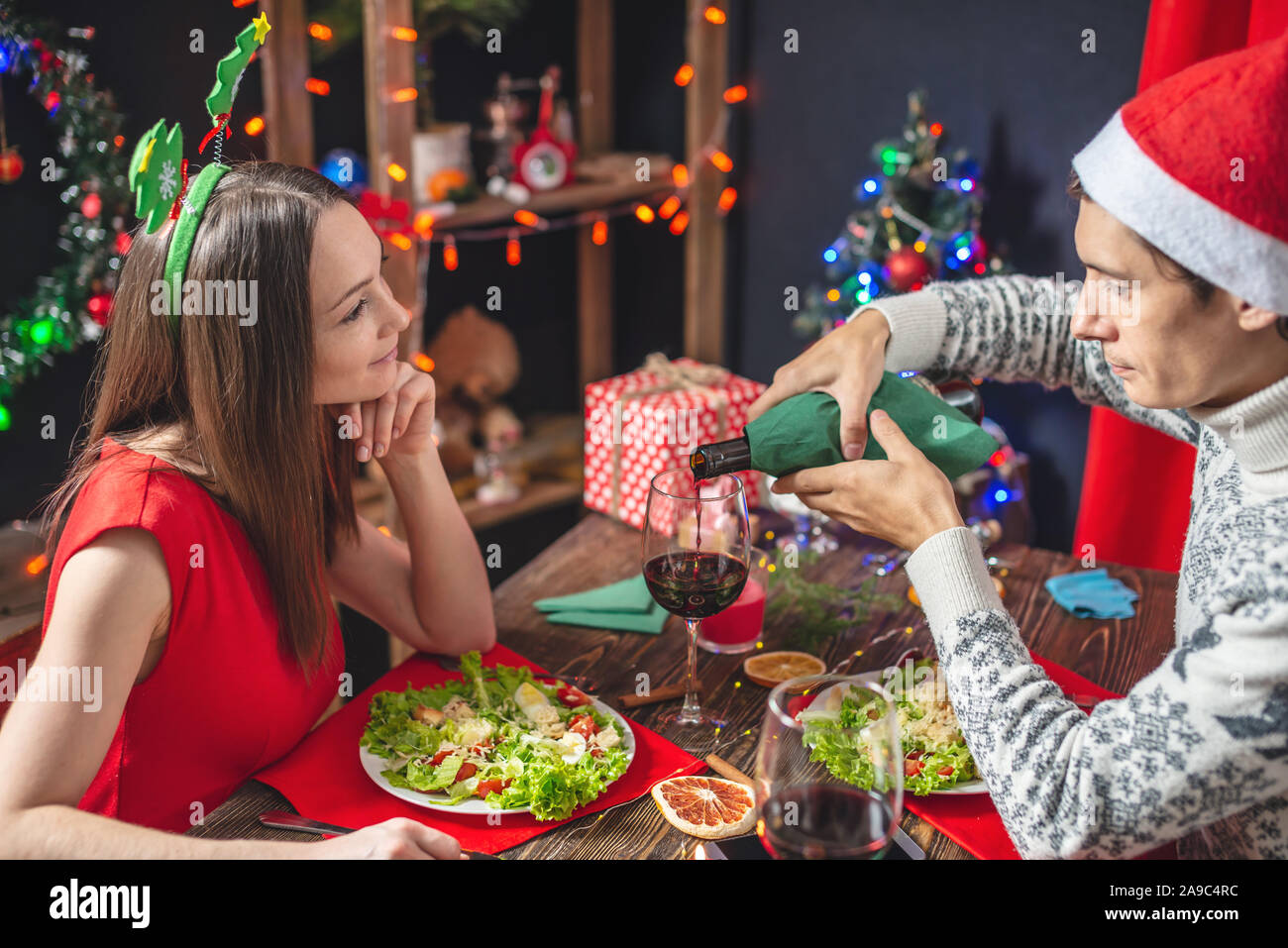 Un giovane bella coppia di amanti trascorrere una serata festiva cenare e bere il vino da occhiali nelle decorazioni di Natale per la vigilia di capodanno. Foto Stock