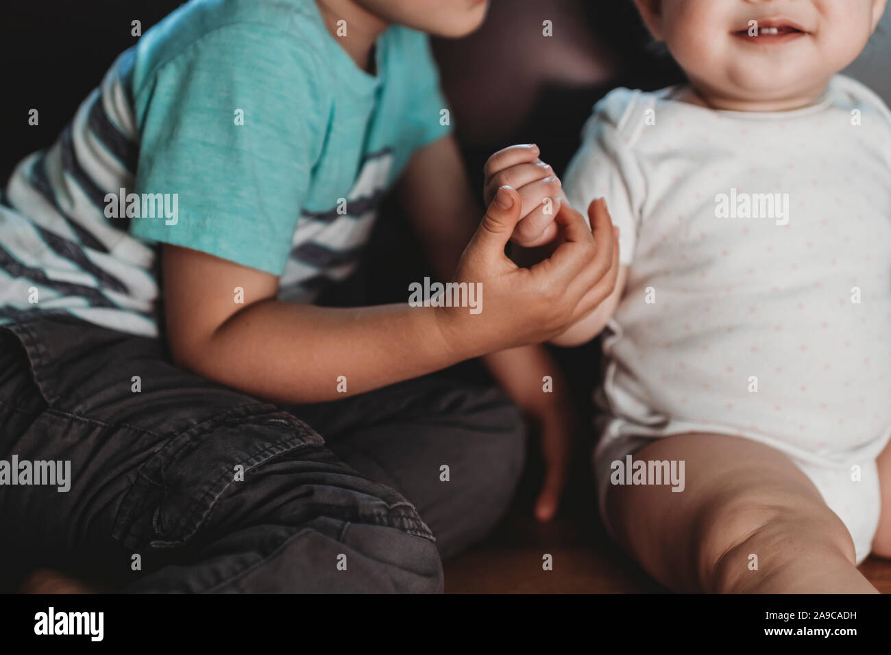 Grande fratello tenendo la mano del bambino sorridente sorella in polkadot Onesie Foto Stock