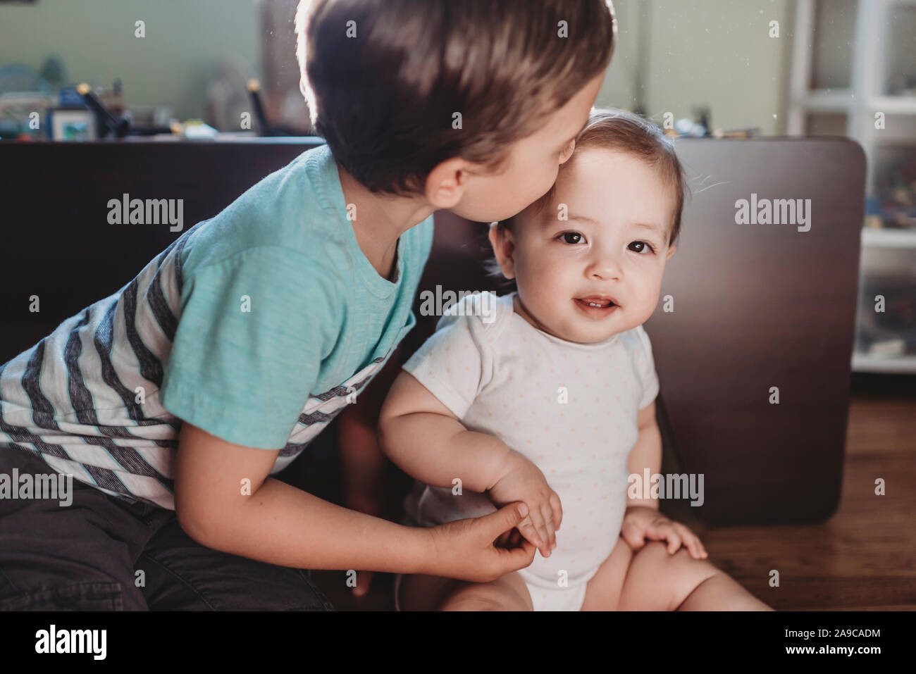 Giovane ragazzo baciare delicatamente la sorella del bambino e tenendo la sua piccola mano Foto Stock