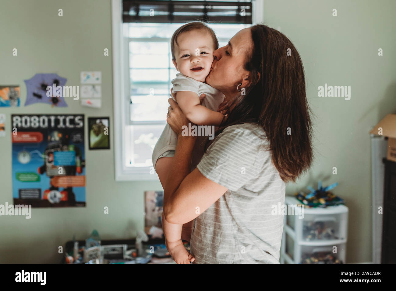 Amare mom kissing sorridente baby nella parte anteriore della finestra in camera giocattolo Foto Stock