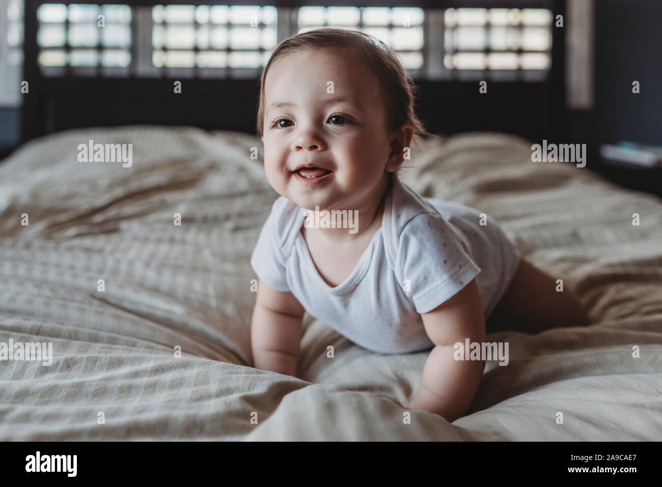 Bambino sorridente con due denti strisciando sul letto in luce dalla finestra Foto Stock
