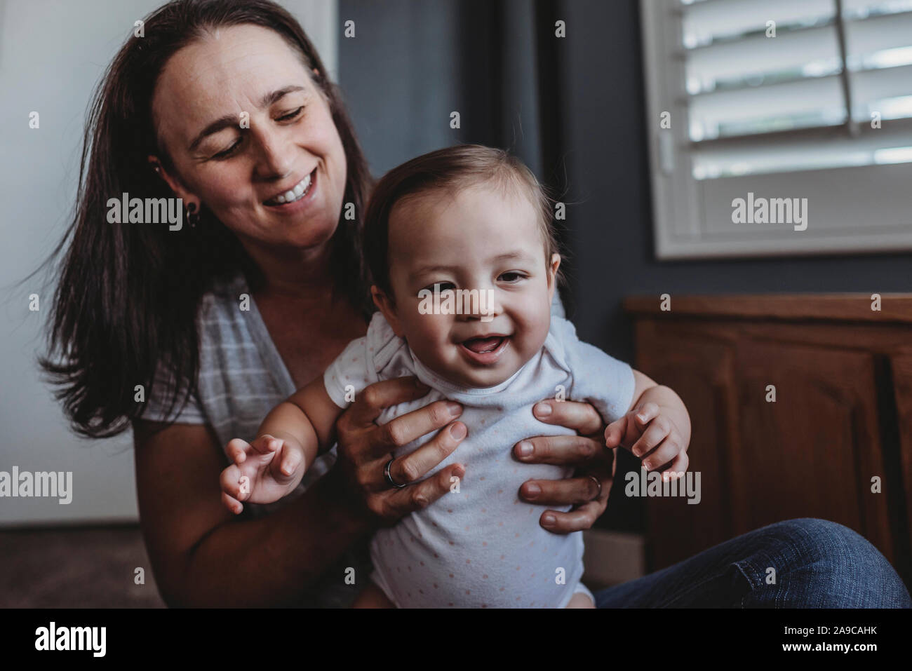 Sorridente mom con capelli lunghi aiutando Laughing baby stand Foto Stock