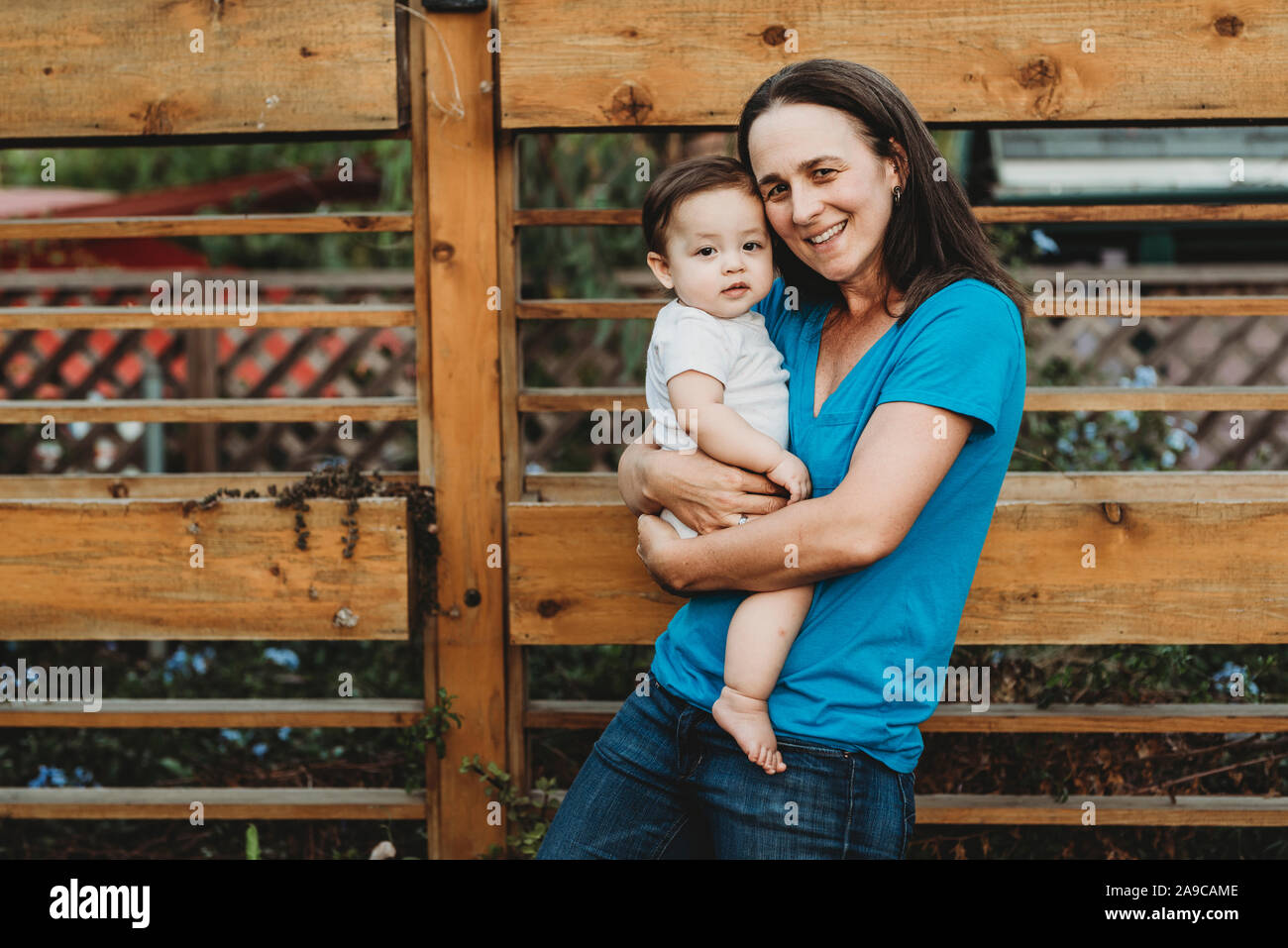 Sorridente mid-40's mom holding bambina all'aperto vicino alla recinzione di legno Foto Stock