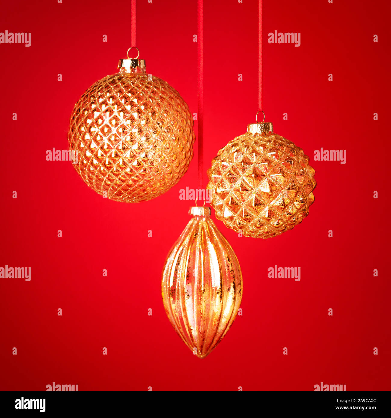 Tre golden baubles di Natale appeso contro lo sfondo rosso. Anno nuovo bigliettino. Messa a fuoco selettiva. Foto Stock