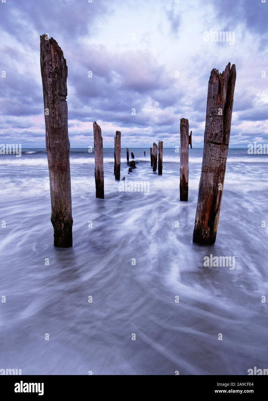 Vista panoramica di pali in legno su una spiaggia, il movimento delle onde è mostrato in aggiunta ad una colorata del cielo della sera - Location: Mar Baltico, Rügen Island Foto Stock