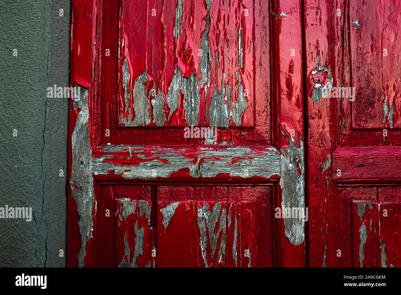 Closeup texture dettagliate di colore rosso brillante vernice scrostata off di una vecchia porta di legno. Panno insinuato in attraverso le crepe nelle pareti. Foto Stock