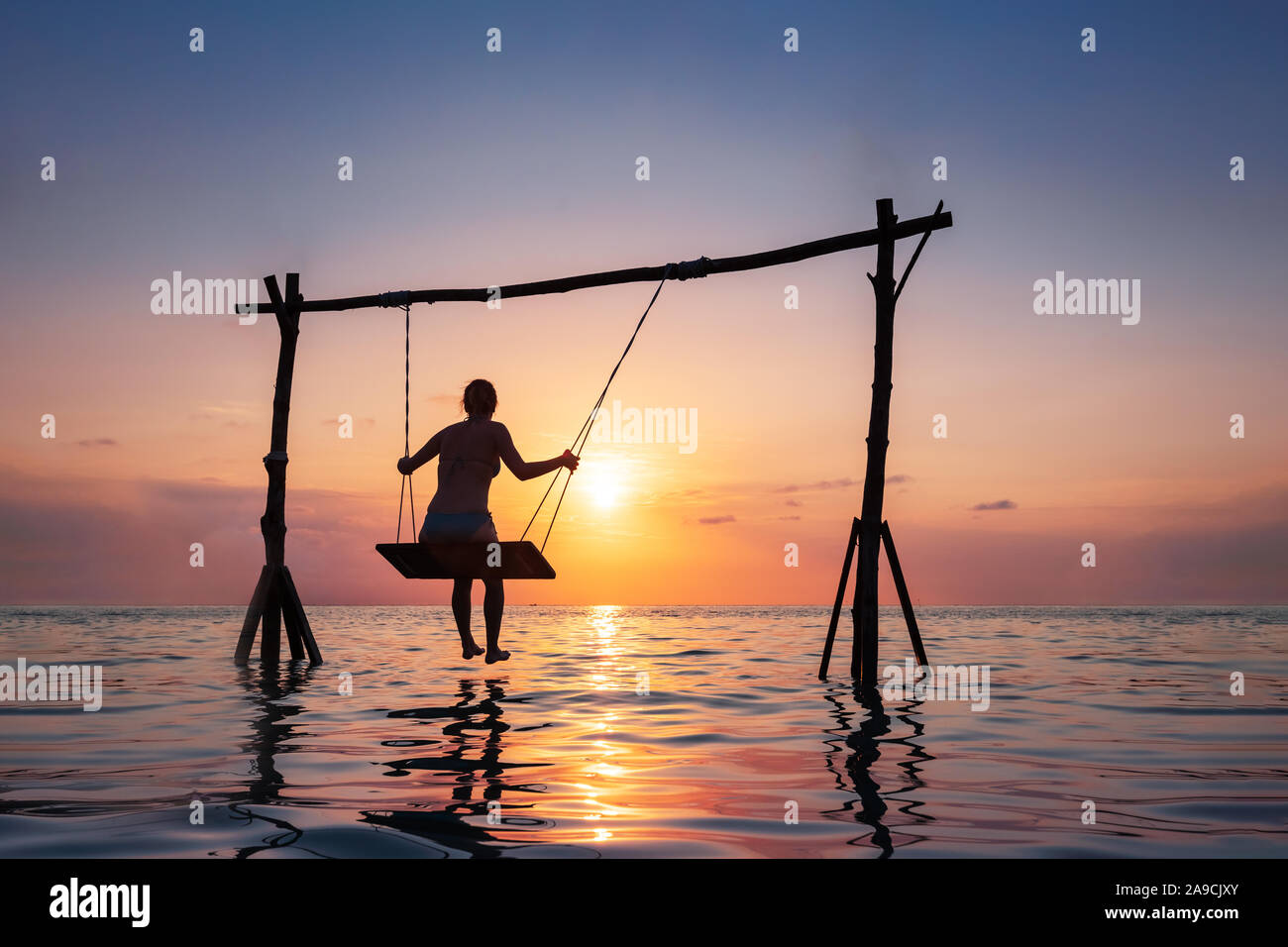 Felice ragazza rilassante sulla spiaggia il swing corda sopra l'acqua di mare al tramonto, Vacanze estive Vacanze resort Foto Stock