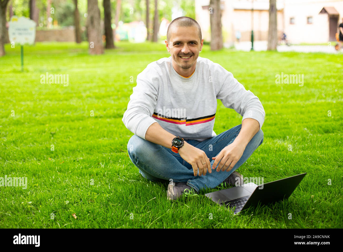 Libero professionista uomo al lavoro su laptop seduto sul prato Foto Stock