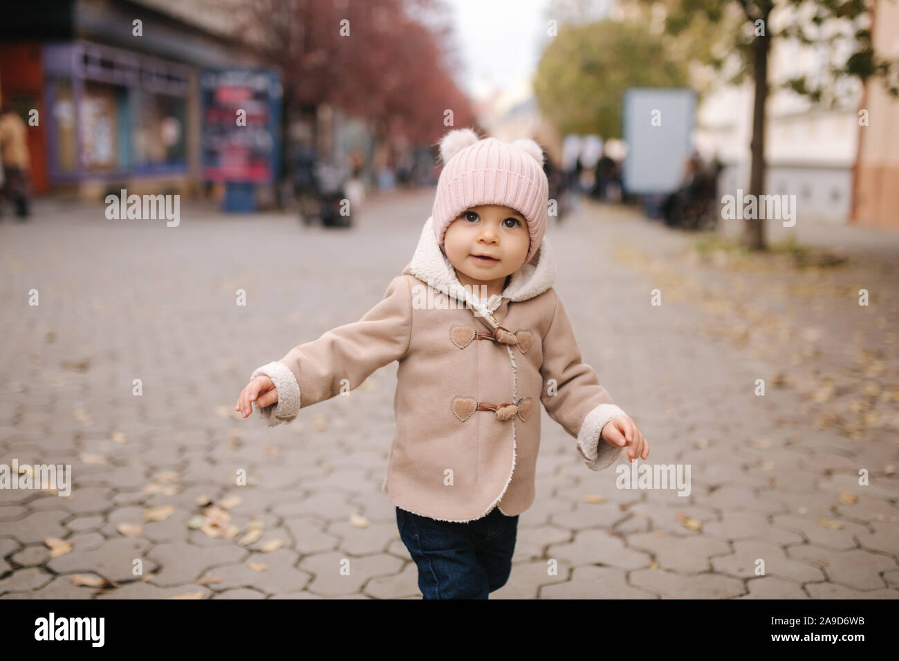 Adorabili poco Baby girl nel bellissimo cappotto marrone a piedi nella città. Carino undici mese baby sorriso ed eseguire Foto Stock