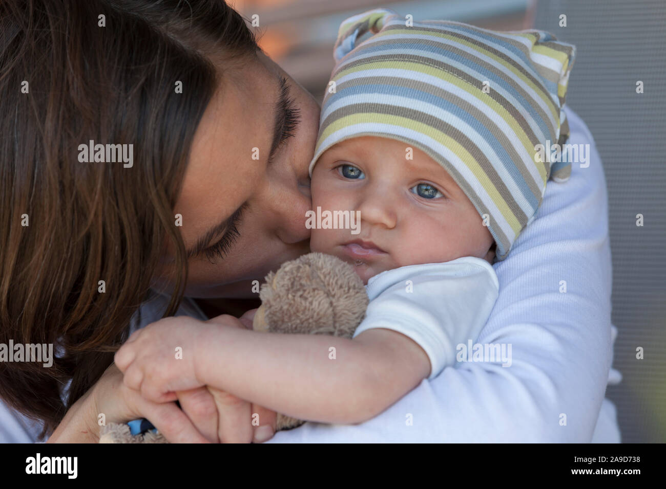Bambino con Teddy nella madre il suo braccio, un bacio sulla guancia in gara i colori Foto Stock