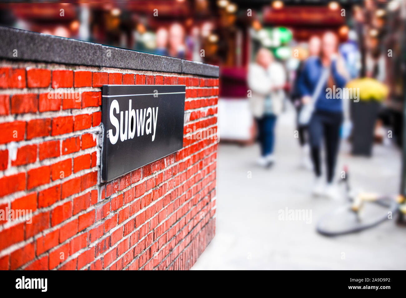 New York City angolo della via di ingresso della metropolitana con il segno sul muro di mattoni e di sfocatura di uomini a piedi in background Foto Stock
