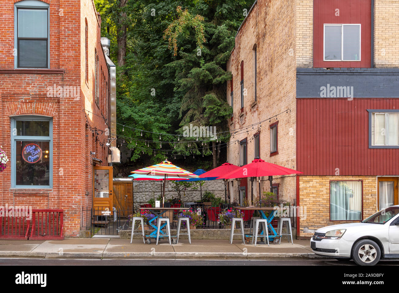 Un piccolo cafe patio con ombrelloni colorati è racchiuso a sandwich tra due edifici in mattoni nella storica cittadina di Wallace, Idaho. Foto Stock